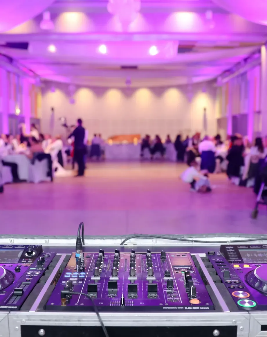 DJ-Pult mit Funkmikrofonen vor einem festlich gedeckten Saal