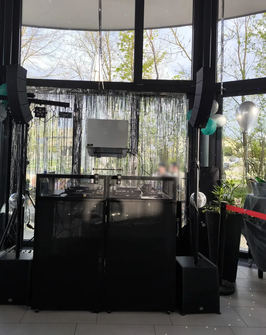 Aufgebautes DJ-Pult mit Boxen und Lichttechnik im Wintergarten bei Tageslicht, dahinter Lametta-Vorhang und Ballons