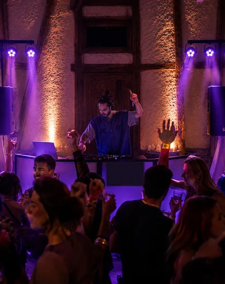 Gäste feiern mit erhobenen Händen vor dem DJ-Pult